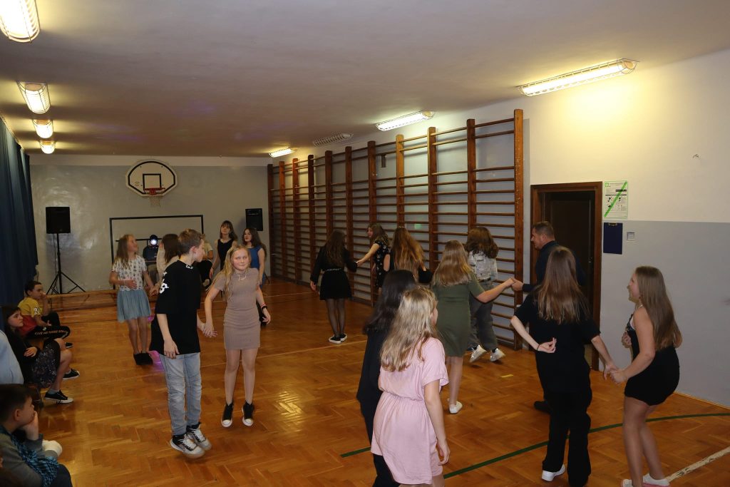 Uczniowie tańczą podczas zabawy choinkowej na sali gimnastycznej.
