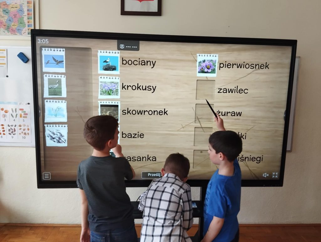 Troje uczniów pracuje na monitorze interaktywnym.
