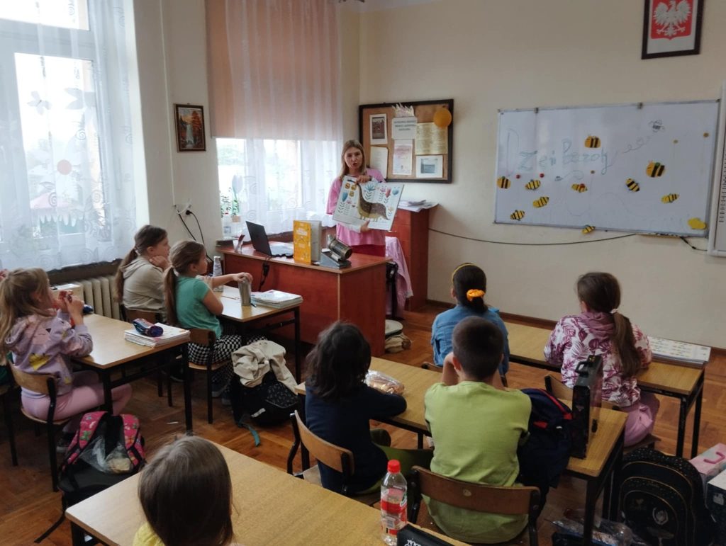 Uczniowie w klasie siedzą w ławkach nauczyciel prezentuje zdjęcie.
